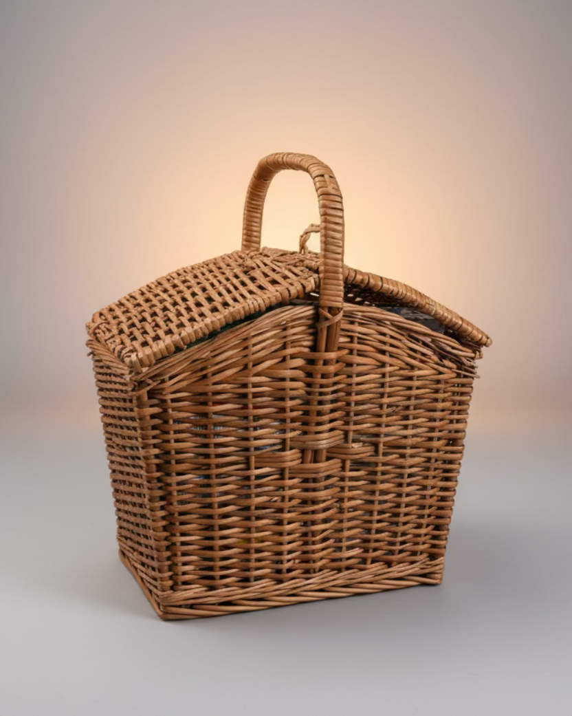 Wicker picnic basket on a concrete floor with a building and various items in the background
