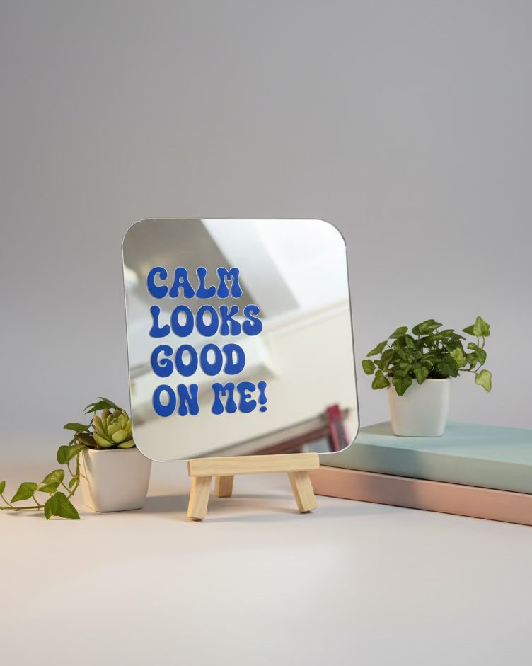 Small mirror with 'CALM LOOKS GOOD ON ME!' text on a desk with various items.